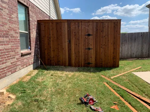 A new tall wooden privacy fence with decorative hinges on the gate, viewed from the backyard.