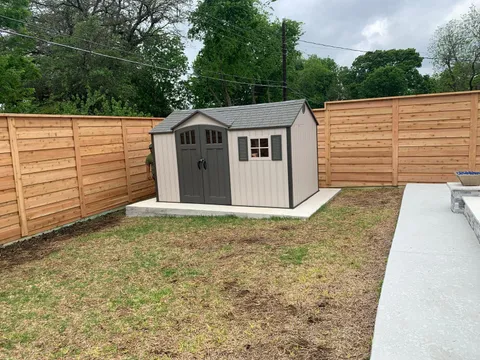 A backyard enclosed by a horizontal wood plank privacy fence, with a shed in the corner.